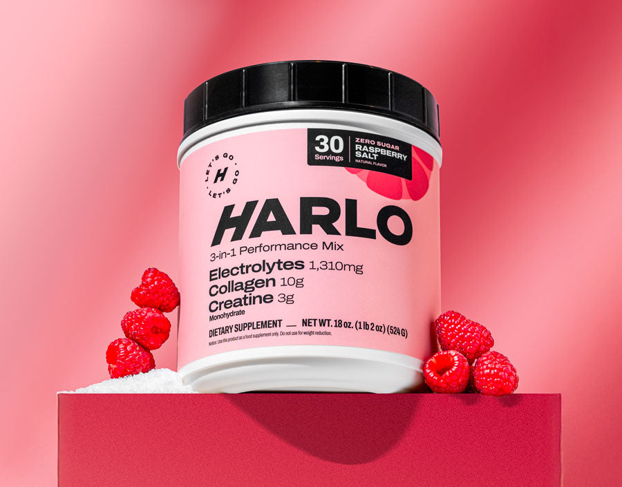 Clean electrolyte powder in raspberry flavor Harlo tub on a pink background with fresh raspberries, perfect for daily hydration.